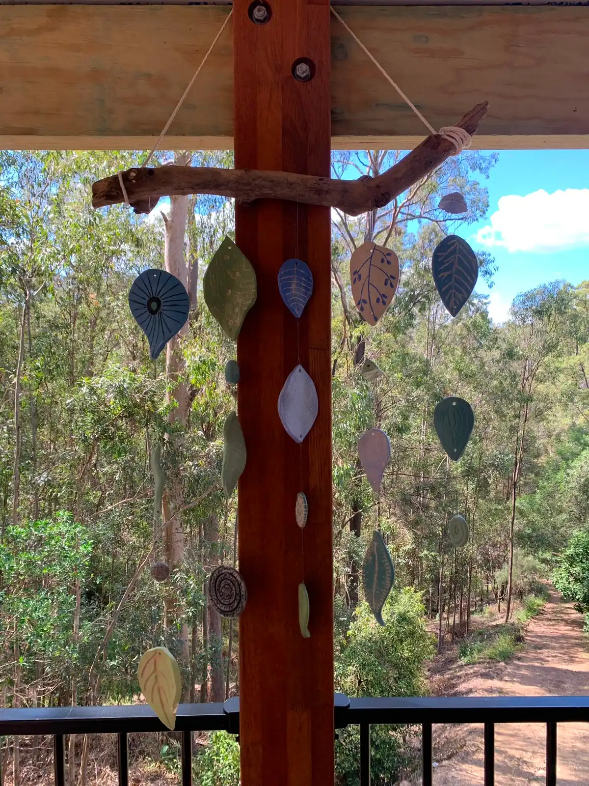Ceramic leaf wind chimes hanging on the studio verandah, with gum trees behind