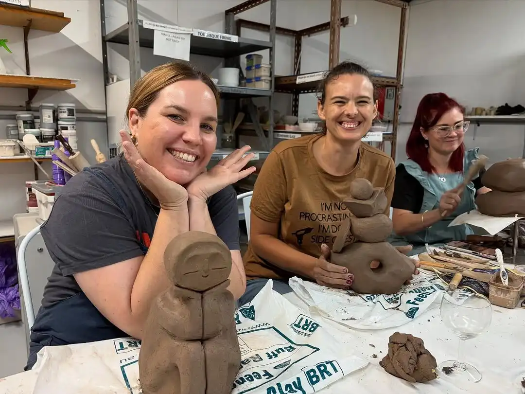 Three friends smiling behind the clay sculptures they made together